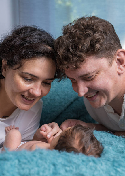 Boldog család egy újszülöttel. Egy szerető anya és apa gyengéden tartja a kisfiát a karjaiban, és gyengéden néz a gyerekre.. - Fotó, kép