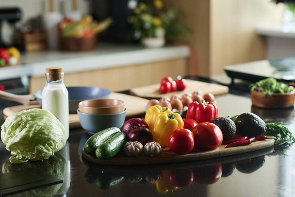 Closeup of set of food on kitchen table, focus on vegetables and bottle of milk - Photo, Image