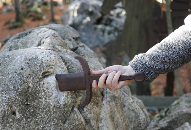 handvat van het zwaard in de steen en de hand van de man die met koppigheid en kracht probeert het eruit te halen - Foto, afbeelding