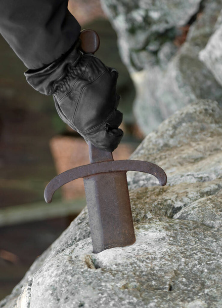 Ręka rycerza próbuje wydobyć miecz z kamienia z wytrwałością i siłą. - Zdjęcie, obraz