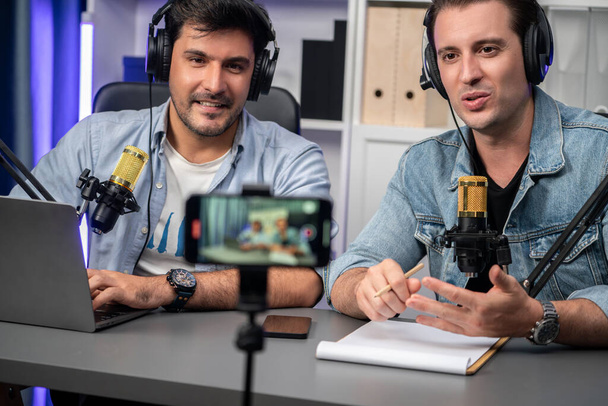Host channel of creative broadcaster living by smartphone in positive podcast with special guest in list script to advice listeners, wearing headsets, using mic radio record at studio. Sellable. - Фото, изображение