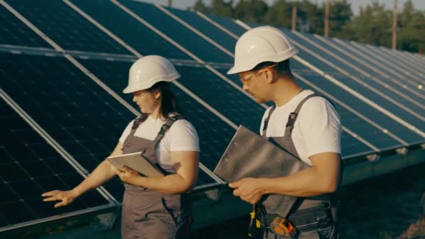 Uma engenheira e seu assistente caminham por painéis solares fotovoltaicos e analisam o resultado da energia verde e da energia renovável.Conceito de energia verde em uma usina de energia solar. - Filmagem, Vídeo