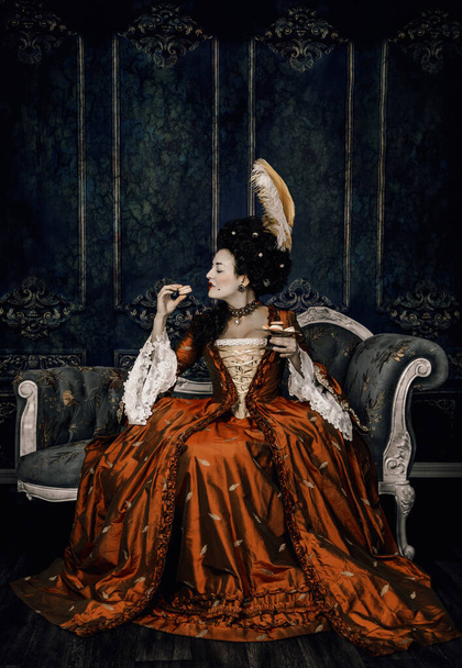 18th century woman wearing a silk gown and sitting on a chaise eating macarons - Photo, Image
