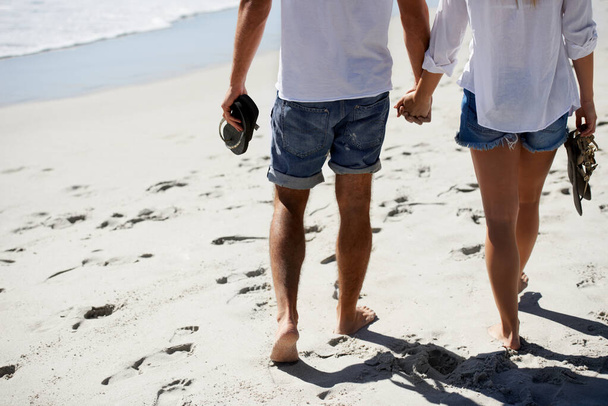 Любовь, взявшись за руки, и пара, гуляющая на пляже на свидание, свидание на свежем воздухе и отпуск. Романтика, мужчина и женщина со спины, ног и отдыха в отпуске вместе с путешествиями, заботой и приключениями - Фото, изображение
