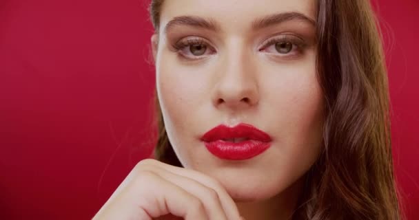Woman, face and confidence wink in studio on red background for beauty flirt, makeup look for cosmetics. Female person, model and portrait as mock up space for lipstick, secret emoji or fun mood. - Footage, Video