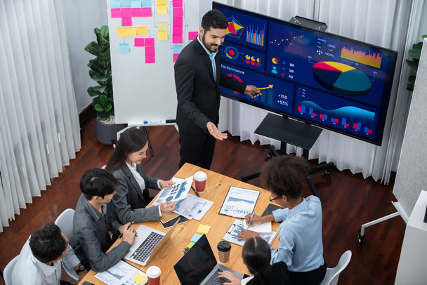 Бизнесмен представляет на экране телевизора дисплей для анализа данных на современном совещании по маркетинговой стратегии. Бизнес-презентация с группой деловых людей в конференц-зале. Конкорд - Фото, изображение