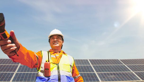 Un technicien principal en électricité remet une perceuse électrique à un collègue de la station solaire inspecte le plan de réparation et d'entretien des panneaux solaires éco-technologiques de la ferme de panneaux solaires. - Photo, image