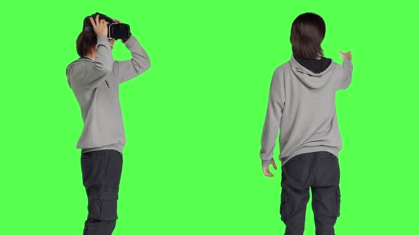 Молодой парень наслаждается устройством виртуальной реальности в студии с зеленым фоном, используя интерактивное зрение на очках. Современный человек развлекается с искусственным интеллектом и гарнитурой. - Кадры, видео