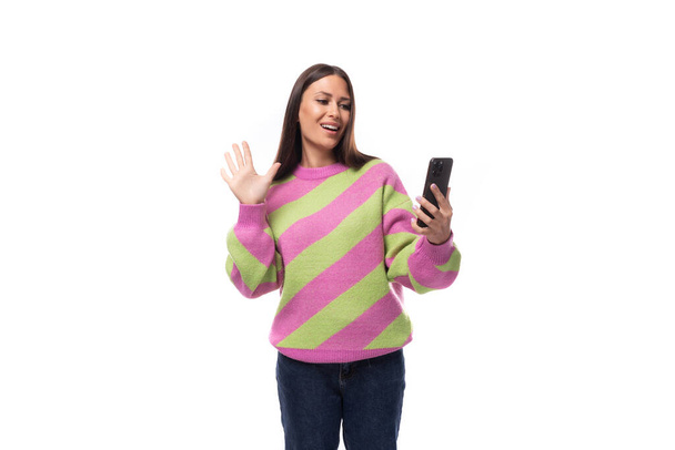młoda ładna kaukaska kobieta z czarnymi włosami ubrana w różowy sweter używa telefonu komórkowego na białym tle. - Zdjęcie, obraz