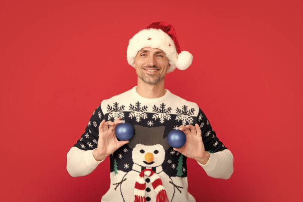 Homme en pull de vacances et chapeau de Père Noël sur fond de studio. Père Noël avec boule, bal de Noël - Photo, image