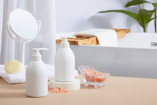 Edessä näkymä merkitsemättömän pumpun pullot näkyvät kylpyhuoneessa päänahan hierontaharjalla ja peili sijoitettu pyyhkeeseen. Vaaleanpunainen himalajan suolalla on antibakteerisia ja anti-inflammatorisia ominaisuuksia - Valokuva, kuva