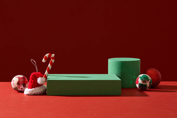 Абстрактный фон для брендинга и минимальная презентация с концепцией Xmas. Милые конфетки, шерстяная шляпа и безделушки, украшенные зелеными подиумами на красном фоне - Фото, изображение