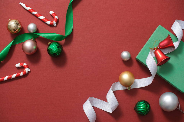 赤い背景に飾られたかわいいバブル,キャンディー缶,鐘,緑の肋骨のトップビュー. クリスマス休日のコンセプト。 デザインのためのコピースペースを備えた最小限のアートバック. フラットレイ - 写真・画像
