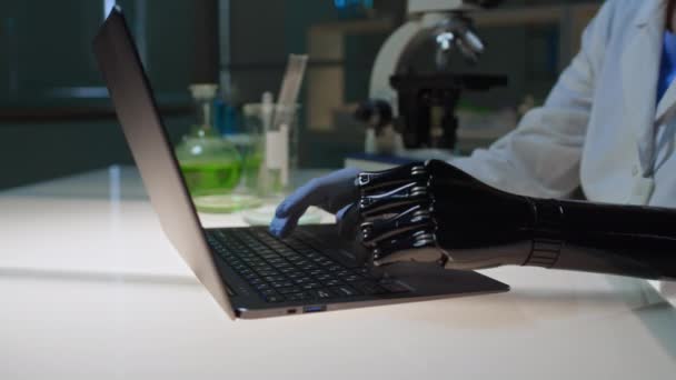 Detailní záběr rukou nerozpoznatelné vědkyně s černou umělou paží hledící do mikroskopu, pak psaní na notebooku, při provádění experimentu v laboratoři - Záběry, video