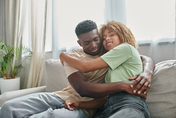 happy african american woman in braces embracing boyfriend while sitting on couch, quality time - Photo, Image
