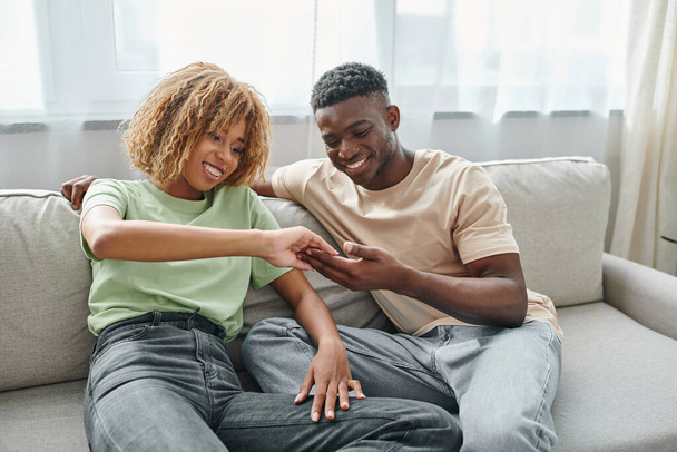 concepto de lenguaje de señas, alegre pareja afroamericana tocando las manos mientras está sentado en el sofá - Foto, Imagen