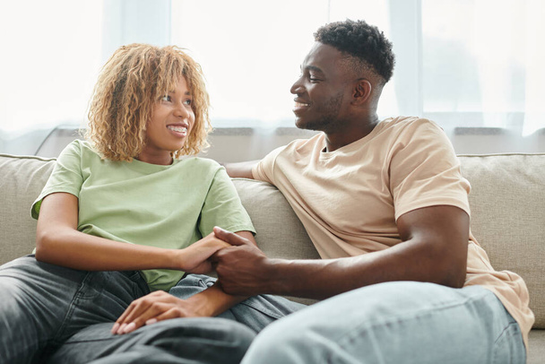 Tender moment tussen Afrikaans Amerikaans koppel thuis, man en vrouw hand in hand in de woonkamer - Foto, afbeelding