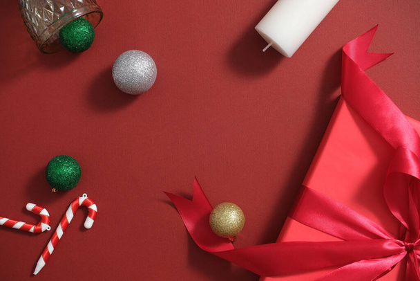 Noel dekorasyonu konsepti. Mum, baston şekerler, takılar ve kırmızı arka planda süslenmiş hediye kutusu. Üst görünüm, ortadaki boşluk tasarım ve kopyalama alanı için - Fotoğraf, Görsel