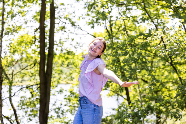 A képen egy fiatal nő látható játékos pózban, kinyújtott karokkal, táncoló vagy forgó erdei környezetben. A gondtalan szelleme ragályos, és a mosolya olyan fényes, mint a foltos. - Fotó, kép