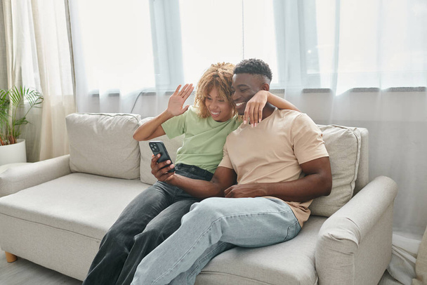 felice coppia africana americana video chat su uno smartphone mentre seduti sul divano insieme - Foto, immagini
