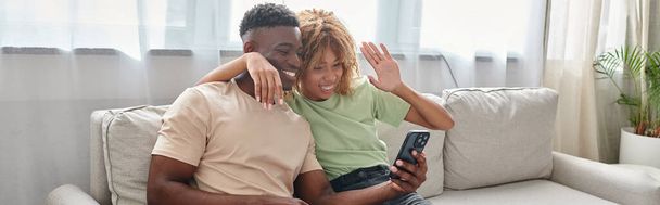 gelukkig Afrikaans amerikaans paar video chatten op een smartphone terwijl zitten op de bank samen, banner - Foto, afbeelding