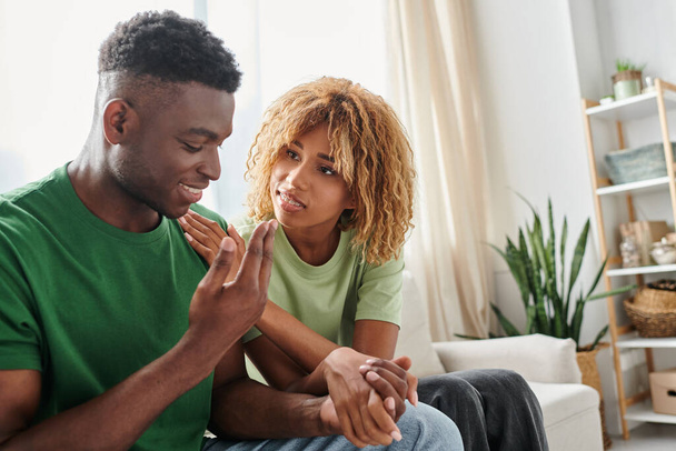 joven afroamericano pareja cogido de la mano mientras sentado juntos en sofá, apoyo emocional - Foto, imagen