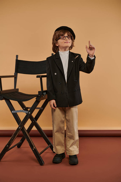 Der inspirierte Junge steht stolz neben dem Regiestuhl, mit einem breiten Lächeln im Gesicht und einem Ideenschild - Foto, Bild