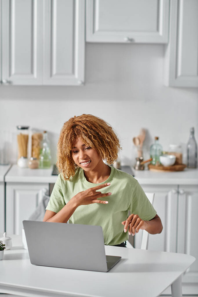 heureux afro-américaine fille dans bretelles en utilisant le langage des signes lors de l'appel vidéo sur ordinateur portable, conversation - Photo, image