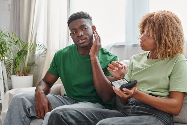afro-americano homem tocando orelha perto namorada segurando dispositivo médico em mãos, aparelho auditivo - Foto, Imagem