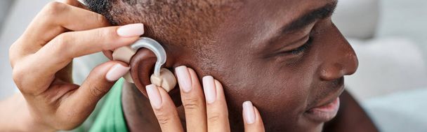 hombre afroamericano feliz sonriendo como su novia ayuda con audífonos, pancarta médica - Foto, imagen