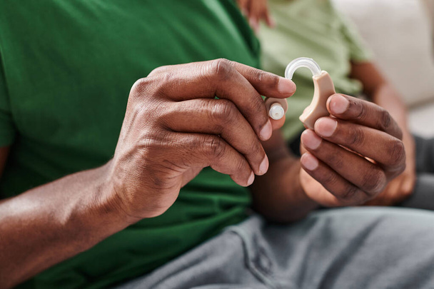 abgeschnittene Aufnahme eines Hörgeräts in den Händen eines schwarzen Mannes, afrikanisch-amerikanische Person mit medizinischem Gerät - Foto, Bild