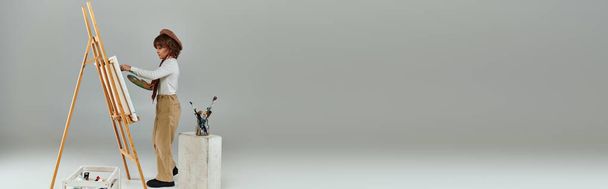 Ahşap sehpanın yanında resim yapan genç bir sanatçı, bereli şık bir çocuk ve palet tutan bir eşarp. - Fotoğraf, Görsel