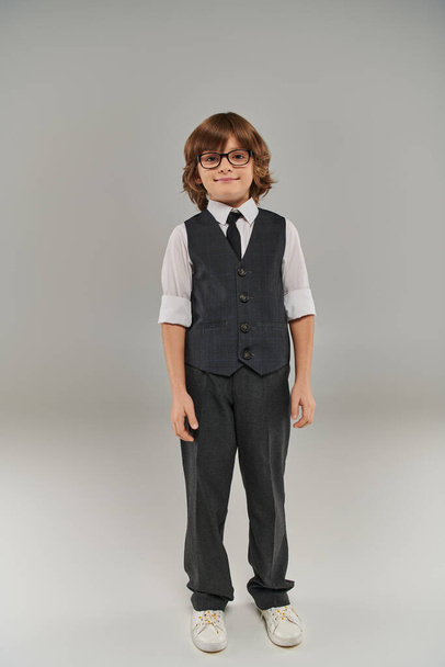przyszły biznesmen, szczęśliwy chłopiec w eleganckim stroju formalnym i okularach stojących na szarym tle - Zdjęcie, obraz