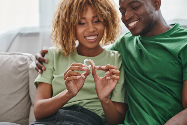 happy african american couple holding hearing aid medical device near boyfriend, accessibility - Photo, Image
