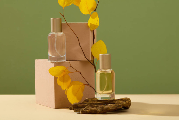 Mockup-Szene für die Werbung für ein Parfümprodukt mit Herbstkonzept. Frontansicht von zwei Glassprühflaschen ohne Etikett auf Würfelpodesten und Stein mit Blättern auf grünem Hintergrund - Foto, Bild