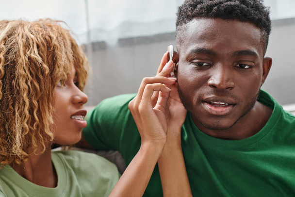mujer afroamericana rizada sosteniendo audífono dispositivo médico cerca de novio, accesibilidad - Foto, imagen