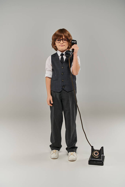 Kravat ve gözlüklü zarif yelek giymiş, gri renkte retro telefon tutan iyi giyimli genç bir beyefendi. - Fotoğraf, Görsel