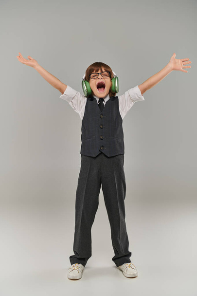 fröhlicher Junge, der triumphierend die Arme hebt, während er über Kopfhörer Musik hört - Foto, Bild