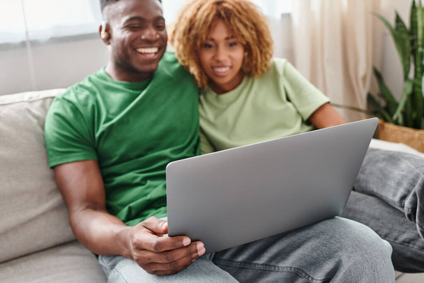 Χαμογελαστό μαύρο ζευγάρι ταινία με τα πόδια στο φορητό υπολογιστή, κουφός άνδρας στην ακοή αέρα και γυναίκα σε τιράντες - Φωτογραφία, εικόνα