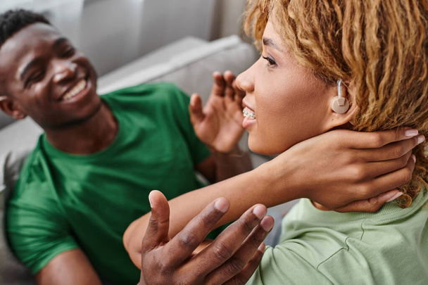 portrait of deaf african american woman in hearing aid device smiling near boyfriend at home - Photo, Image