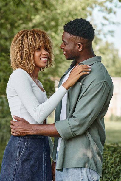 feliz pareja afroamericana cogida de la mano y abrazándose al aire libre, mujer con frenillos - Foto, Imagen