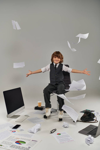 happy boy in formal attire sitting near documents in air and office supplies, future professional - Photo, Image
