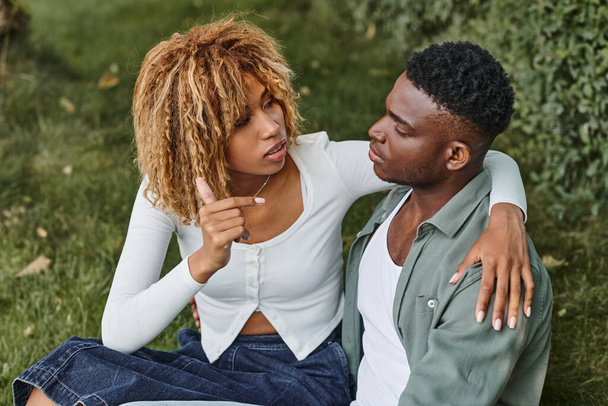 jovem casal afro-americano usando linguagem de sinais para a comunicação enquanto sentado na grama - Foto, Imagem