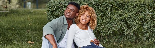 陽気なアフリカ系アメリカ人のカップルが抱擁し,緑の草の上に座って幸せの旗 - 写真・画像