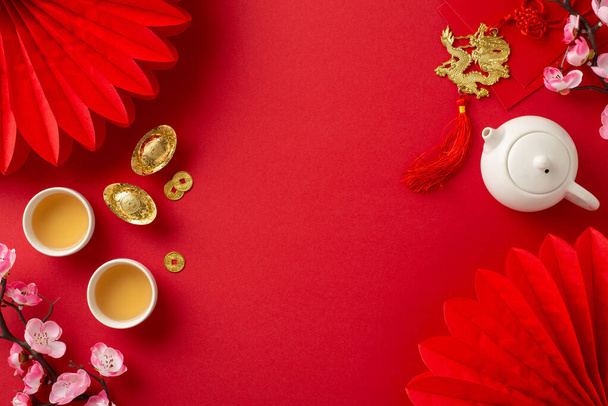 Lunar New Year tea ceremony top view setting featuring Feng Shui elements, teapot set, and green tea for a family ritual. Paper fans and orchids adorn the red backdrop, creating a festive atmosphere - Photo, Image