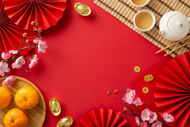 China's festive New Year spread: Overhead shot of traditional items, green tea ceremony set, bamboo placemat, plate with tangerines, sakura on vibrant red background, providing space for text or ads - Photo, Image