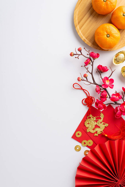 Исследуйте эту китайскую новогоднюю сцену: верхний вид вертикальный снимок вентилятора, древние монеты, счастливый sycee, красный Hong Bao, дракон шарм повешение, мандарин заполнены тарелку, сакура, белый фон с пространством для текста - Фото, изображение
