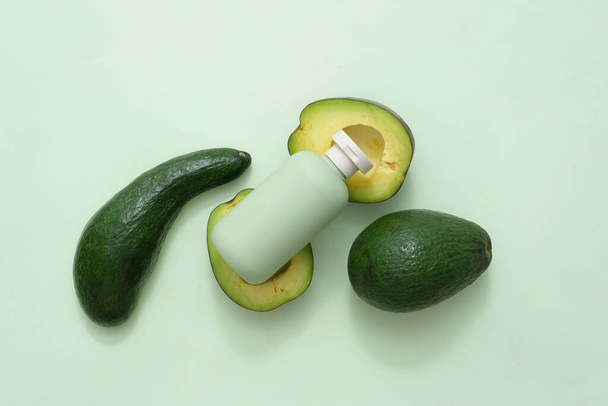 Scena makowa do reklamy kosmetyków ze składnikiem z awokado. Na zielonym tle zielona butelka ze świeżymi awokado i połówkami awokado. Widok z góry, przestrzeń do projektowania - Zdjęcie, obraz