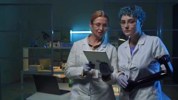 Ritratto medio di due scienziate caucasiche, di mezza età con tablet e giovani con braccio protesico, che posano insieme in laboratorio di chimica, guardando la fotocamera con fiducia - Filmati, video