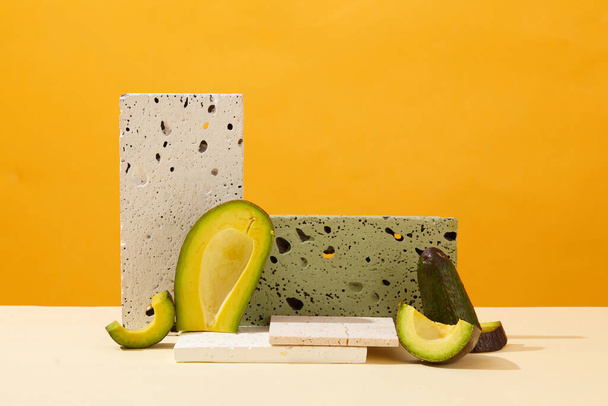 Minimalistischer Hintergrund für Präsentationskosmetik mit Avocado-Extrakt. Frische Scheiben Avocado und graue Ziegel Podeste auf gelbem Hintergrund dekoriert. Frontansicht - Foto, Bild